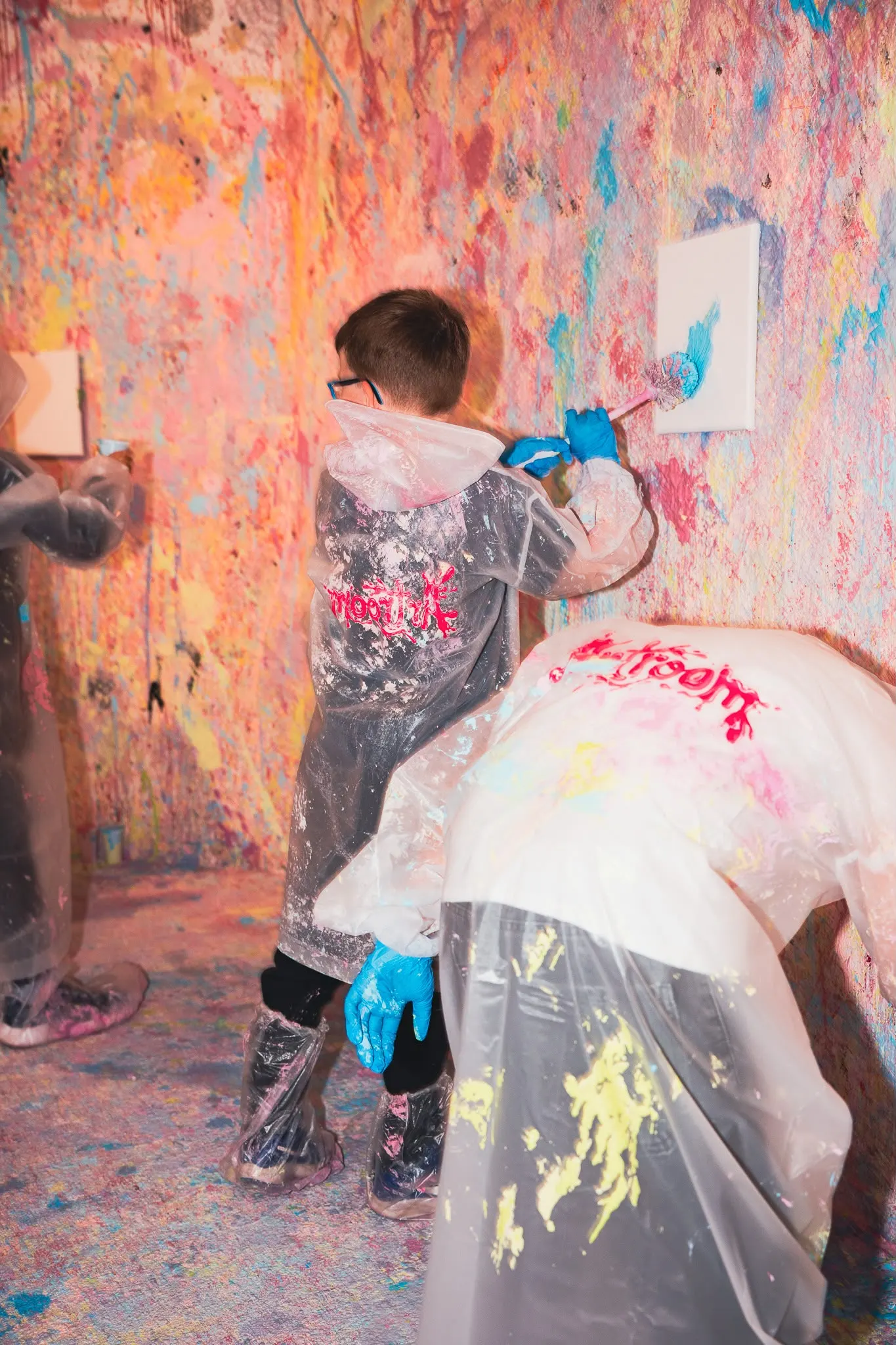 Kinder in Schutzanzügen malen mit Pinseln an der bunten Wand