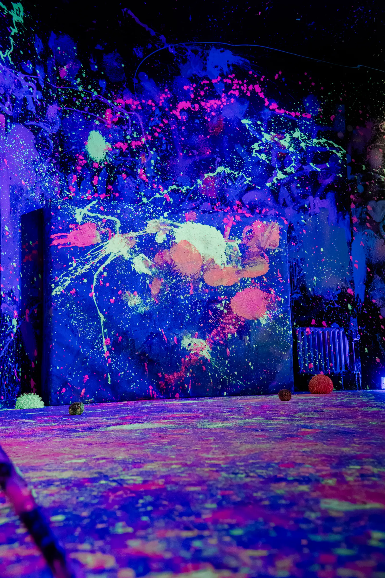 Neon Rage Room im Schwarzlicht mit leuchtenden Farbspritzern und Bällen auf dem Boden