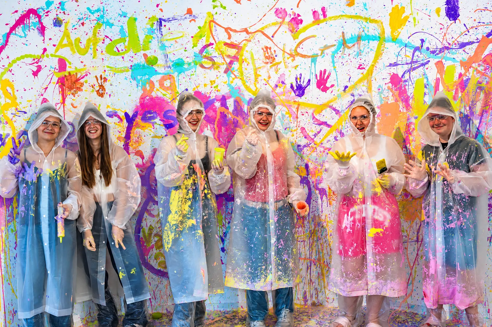 Gruppe in Schutzanzügen lacht vor der bunt bemalten Wand im Splash Room